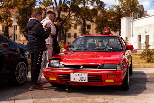 a-group-of-people-standing-around-a-red-car